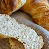 Ein aufgeschnittenes Dinkelbrötchen zeigt die mittelporige, helle Krume und dünne, goldbraun ausgebackene Kruste.