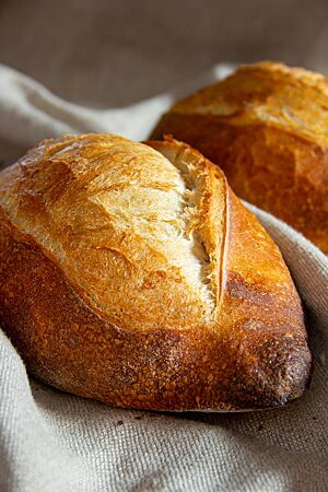 Zwei goldbraun ausgebackene Pain maison de tradition mit rustikal aufgerissener Krume liegen auf einem Leinentuch.