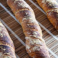 Drei verdrehte Brotstangen mit dunkel ausgebackener, rustikaler Kruste liegen auf einem Tisch.