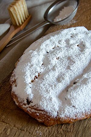 Ein flacher, breiter Stollen mit einer dicken Puderzuckerhaube liegt auf einem Holzbrett.