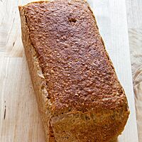 Das in der Kastenform gebackene Wanderbrot mit glatter Kruste liegt auf einem hellen Holztisch.