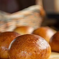 Die goldbraun ausgebackenen DDR-Milchbrötchen mit glänzender Kruste liegen auf einem Holztisch.