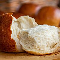 Ein auseinandergebrochenes Milchbrötchen zeigt die wattig-weiche, feinporige Krume umgeben von der hauchdünnen Kruste.