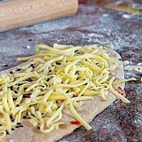 Ein länglich ausgerollte Teigling ist mit schwarzem Sesam und geriebenem Gouda bestreut.