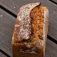 Das kräftig ausgebackene, rustikal aufgerissene Dinkelmischbrot mit leicht bemehlter Kruste liegt auf einem Holztisch.