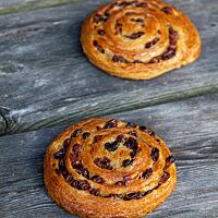 Zwei zur Schnecke geformte, goldbraun ausgebackene Pain aux raisins liegen auf einem rustikalen Holztisch.