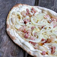 Der knusprig ausgebackene Flammkuchen ist mit Zwiebeln und Speck belegt.