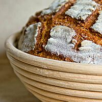 Das kräftig ausgebackene, bemehlte Buttermilchbrot liegt mit rautenförmig eingeschnittener Kruste in einem Gärkorb aus Peddigrohr.