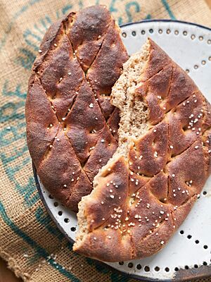 Das dunkel ausgebackene Fladenbrot mit rautenförmig eingeschnittener Oberfläche ist mit grobem Salz bestreut.