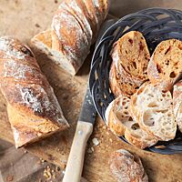 In einem Körbchen liegen mehrere Scheiben des grobporigen, luftigen Restaurantbrotes. Bei einigen ist die Krume rötlich gefärbt und enthält getrocknete Tomatenstücke.