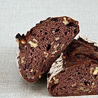 Das kräftig ausgebackene, rustikal aufgerissene Rotkorn-Nussbrot zeigt im Anschnitt seine dunkle, lockere Krume mit grob gehackten Walnüssen.