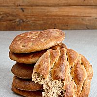 Mehrere goldbraun ausgebackene Pitas liegen übereinandergestapelt auf einem Leinentuch.