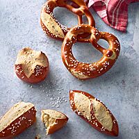 Mit Salz bestreutes Laugengebäck als Brezel, Stangen oder Brötchen geformt, liegt auf einer Arbeitsfläche.
