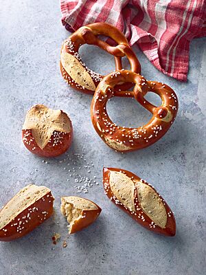 Mit Salz bestreutes Laugengebäck als Brezel, Stangen oder Brötchen geformt, liegt auf einer Arbeitsfläche.