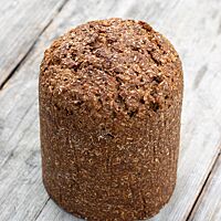 Ein Schwarzbrot in Pollerform steht auf einem rustikalen Holztisch.