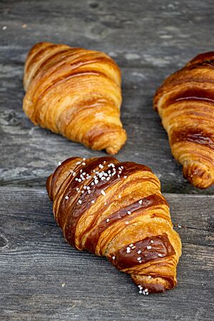Goldbraun ausgebackene Croissants liegen auf einem rustikalen Holztisch.