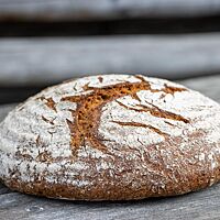 Das runde Einkornbrot mit stark bemehlter, leicht aufgerissener Kruste liegt auf einem rustikalen Holztisch.