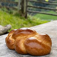 Der goldbraun ausgebackene Zopf mit glänzender Oberfläche liegt auf einem rustikalen Holztisch.