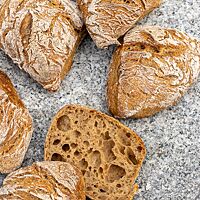 Ein aufgeschnittenes Weizenmischbrötchen zeigt die mittelbraune Krume mit wilder Porung, umgeben von der kräftig ausgebackenen, krossen Kruste.