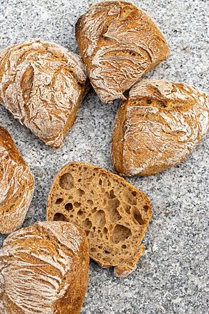 Ein aufgeschnittenes Weizenmischbrötchen zeigt die mittelbraune Krume mit wilder Porung, umgeben von der kräftig ausgebackenen, krossen Kruste.