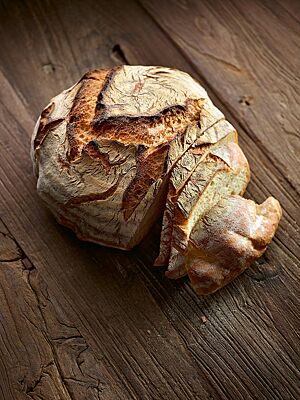 Der runde Laib des Weizenbrotes hat eine rustikal aufgerissene, kräftig ausgebackene Kruste und eine helle, lockere Krume.