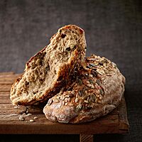 Der von Hand in zwei Hälften gerissene Laib hat eine mit gemischten Saaten bestreute Kruste und eine hellbraune, mit Saaten gespickte Krume.