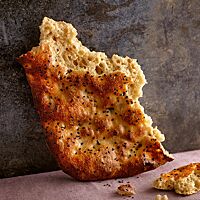 Das kräftig ausgebackene Dinkelfladenbrot mit grobporiger Krume ist auf der Oberfläche mit schwarzem Sesam bestreut.