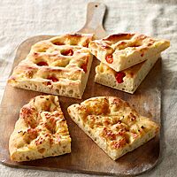 Die in mehrere Stück geschnittene Focaccia ist mit Tomatenstücken belegt und hat eine deutlich eingedrückte Oberfläche.