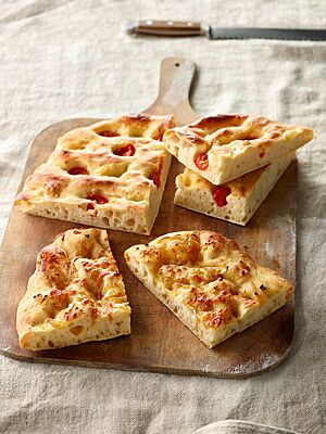Die in mehrere Stück geschnittene Focaccia ist mit Tomatenstücken belegt und hat eine deutlich eingedrückte Oberfläche.