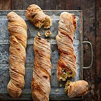 Drei kräftig ausgebackene, in sich verdrehte Wurzelbrote liegen auf einem Blech (links: ohne Füllung, mittig: mit Walnüssen in der lockeren Krume, rechts: mit Oliven und Käse gefüllt).