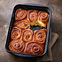 Neun goldbraun ausgebackene Zimtschnecken liegen in einer Auflaufform und zeigen in ihren Windungen die Füllung aus Butter und Zimtzucker.