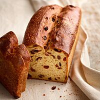 Das in einer Kastenform gebackene Rosinenbrot mit glänzender, goldbraun ausgebackener Kruste zeigt im Anschnitt seine hellgelbe, kleinporige und großzügig mit Rosinen bestückte Krume.