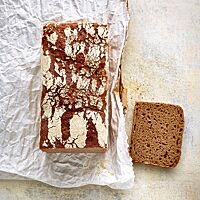 Das Dreikornvollkornbrot wurde in einer Kastenform gebacken und hat eine fein gemaserte, weiß bemehlte Kruste und eine dunkelbraune, lockere Krume.