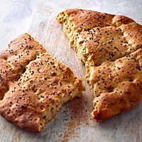 Das glänzend-braune Fladenbrot mit Schwarzkümmelsamen auf der Oberfläche hat eine hellgelbe, kleinporige Krume.