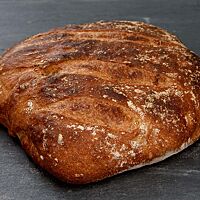 Das Weizenbrot aus weichem Teig hat eine kräftig ausgebackene, leicht glänzende Kruste mit Mehlspuren auf der Oberfläche.