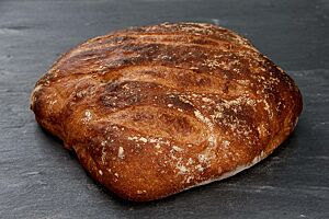 Das Weizenbrot aus weichem Teig hat eine kräftig ausgebackene, leicht glänzende Kruste mit Mehlspuren auf der Oberfläche.