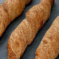 Drei in feinem Weizenschrot gewälzte Brotwurzeln liegen auf einer dunklen Arbeitsfläche.