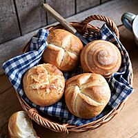 Das runde, kräftig ausgebackene Joghurtbrötchen mit spiralförmigem Ausbund (rechts oben) liegt neben einer Münchener Mundsemmel (links oben) sowie einer Rosensemmel (links unten) und einer Kaisersemmel (rechts unten) in einem geflochtenen Brotkorb.
