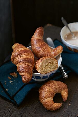 Pariser Gipfel (oben rechts), Bamberger Hörnla (unten) und Croissants (oben links) liegen in einem weißen Schälchen. Die leicht gebogenen Pariser Gipfel haben eine goldbraun ausgebackene, glänzende Kruste und eine feinblättrige, buttrige Krume.