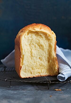 Eine an der Kontaktstelle auseinandergebrochene Brioche liegt auf einem dunklen Gitterrost. Die helle, wattige Krume wird von einer feinen Krume umgeben.