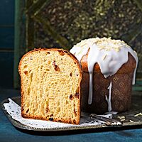 Ein ganzer und ein halbierter Kulitsch stehen auf einer silbernen Platte. Die Krume des Kulitsch ist sehr wattig, weich und mit Sultaninen, Zitronat und Orangeat durchzogen. Die glatte, glänzende Kruste wurde mit einer dicken Zuckerguss-Schicht überzogen und mit Mandelstiften bestreut.