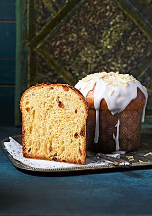 Ein ganzer und ein halbierter Kulitsch stehen auf einer silbernen Platte. Die Krume des Kulitsch ist sehr wattig, weich und mit Sultaninen, Zitronat und Orangeat durchzogen. Die glatte, glänzende Kruste wurde mit einer dicken Zuckerguss-Schicht überzogen und mit Mandelstiften bestreut.