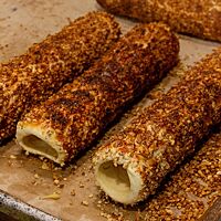 Fünf goldbraun ausgebackene und bereits von der Holzstange abgezogene Skalický Trdelník mit Walnüssen auf der Oberfläche liegen auf Backpapier.