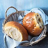 In einem Holzkorb, der mit einem hellgrauen Tuch ausgelegt ist, liegen ein Milchbrot und ein Rosinenbrot. Beide haben eine sehr wattig-weiche Krume und eine goldbraun ausgebackene, glänzende, zarte Kruste.