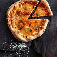 Eine mit Tomatensauce, Mozzarella und Basilikum belegte Pizza Margherita zeigt ihren hellbraun ausgebackenen, knusprigen Rand.