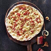 Der knusprig ausgebackene klassische Flammkuchen ist mit Crème fraîche, Bauchspeck und Zwiebeln belegt.