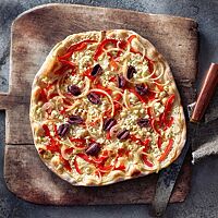 Der knusprig ausgebackene Flammkuchen mit Sauerteig ist mit Crème fraîche, Paprika, Zwiebeln, Oliven und Feta belegt.