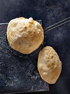 Zwei knusprig frittierte, aufgeblähte Bhatura zeigen ihre goldgelbe Kruste.