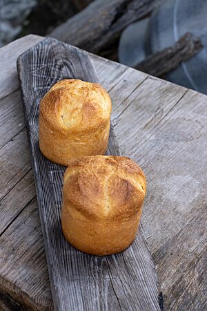 Goldbraun ausgebackene Brioches mit kreuzförmigem Einschnitt stehen auf einem verwitterten, rustikalen Holzbrett.