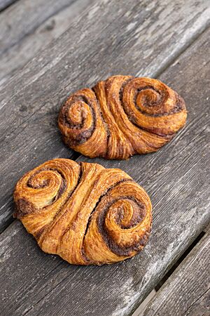Zwei goldbraun ausgebackene Franzbrötchen mit karamellisierter Zimtzuckerfüllung liegen auf einem rustikalen Holztisch.